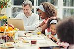 Smiling young multi-ethnic family using laptop and eating breakfast at table