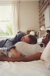 Affectionate pregnant couple cuddling and napping on bed