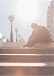 Male runner tying shoes on sunny urban stairs