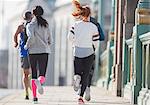 Runners running on sunny urban sidewalk