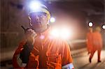 Male foreman with headlamp using walkie-talkie at dark construction site