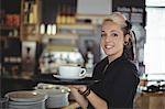 Portrait of waitress standing with cup of coffee in cafe