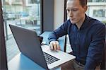 Male executive using laptop at counter in cafeteria