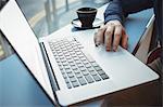 Mid-section of male executive using laptop in cafeteria