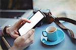 Hands of male executive holding mobile phone while having coffee in cafeteria