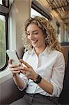 Smiling woman using mobile phone inside train compartment