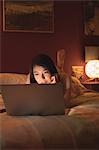 Woman lying and using laptop on bed in bedroom