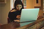 Woman using mobile phone and laptop on kitchen counter at home