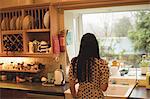 Rear view of woman looking through window in kitchen at home