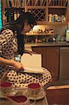 Woman sitting on kitchen worktop and reading book at home