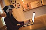 Woman using virtual reality headset while typing on laptop at home