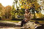 Woman using mobile phone while sitting on a tree trunk in park