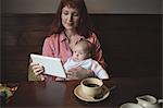 Mother with her baby using digital tablet in café