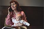 Mother with her baby talking on mobile phone in café