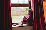 Thoughtful girl sitting on window sill at home