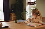 Thoughtful girl sitting at table while studying in living room at home