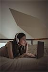 Woman with headphones using laptop on bed at home