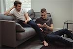 Gay couple using digital tablet and mobile phone in living room at home