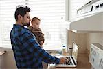 Father using laptop while holding his baby in kitchen at home