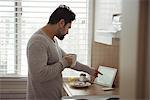 Man using digital tablet while having coffee in kitchen