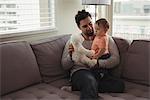 Father and baby playing with teddy bear on sofa in living room at home