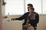 Father holding his baby while using laptop at desk at home