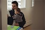 Father holding his baby while using digital tablet at desk in home