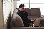 Man talking on mobile phone while using laptop on sofa at home