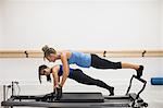 Female trainer assisting group of woman with stretching exercise on reformer in gym