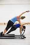 Female trainer assisting woman with stretching exercise on reformer in gym