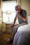 Senior man using a tissue to blow his nose in the bedroom at home