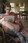 Woman sitting and using digital tablet on couch in living room at home