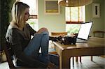 Woman using laptop while sitting in living room at home