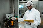 Confident male worker holding clipboard while operating machine in juice factory
