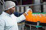 Male worker checking orange juice bottles in factory