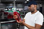 Young male worker inspecting juice bottle in factory