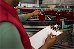 Mid section of male worker inspecting red juice bottles on production line in factory