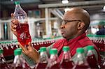Serious male worker examining bottle in cold drink factory