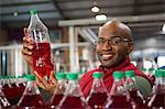 Portrait of smiling male worker showing juice bottle in factory