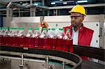 Confident male employee inspecting bottles in juice factory