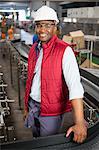 Portrait of happy male employee standing by conveyor belt in factory