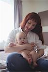 Smiling mother with baby sitting on bed at home