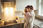 Loving mother carrying baby in kitchen