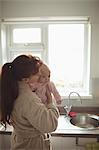 Loving mother kissing baby in kitchen at home