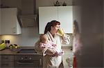 Mother carrying baby while having coffee in domestic kitchen