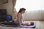 Full length of happy mother exercising while looking at baby on yoga mat