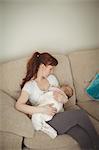 High angle view of mother breastfeeding baby on sofa at home