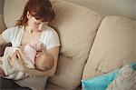 Loving mother breastfeeding baby on sofa in living room at home