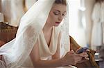 Young bride using mobile phone on sofa in boutique