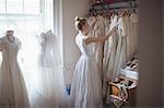 Young bride selecting wedding dress from clothes hanger in a boutique